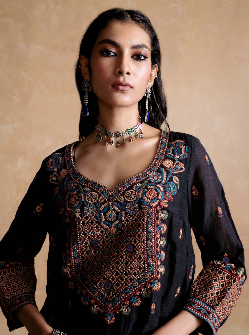 Woman wearing a black embroidered top with colorful patterns on a beige background