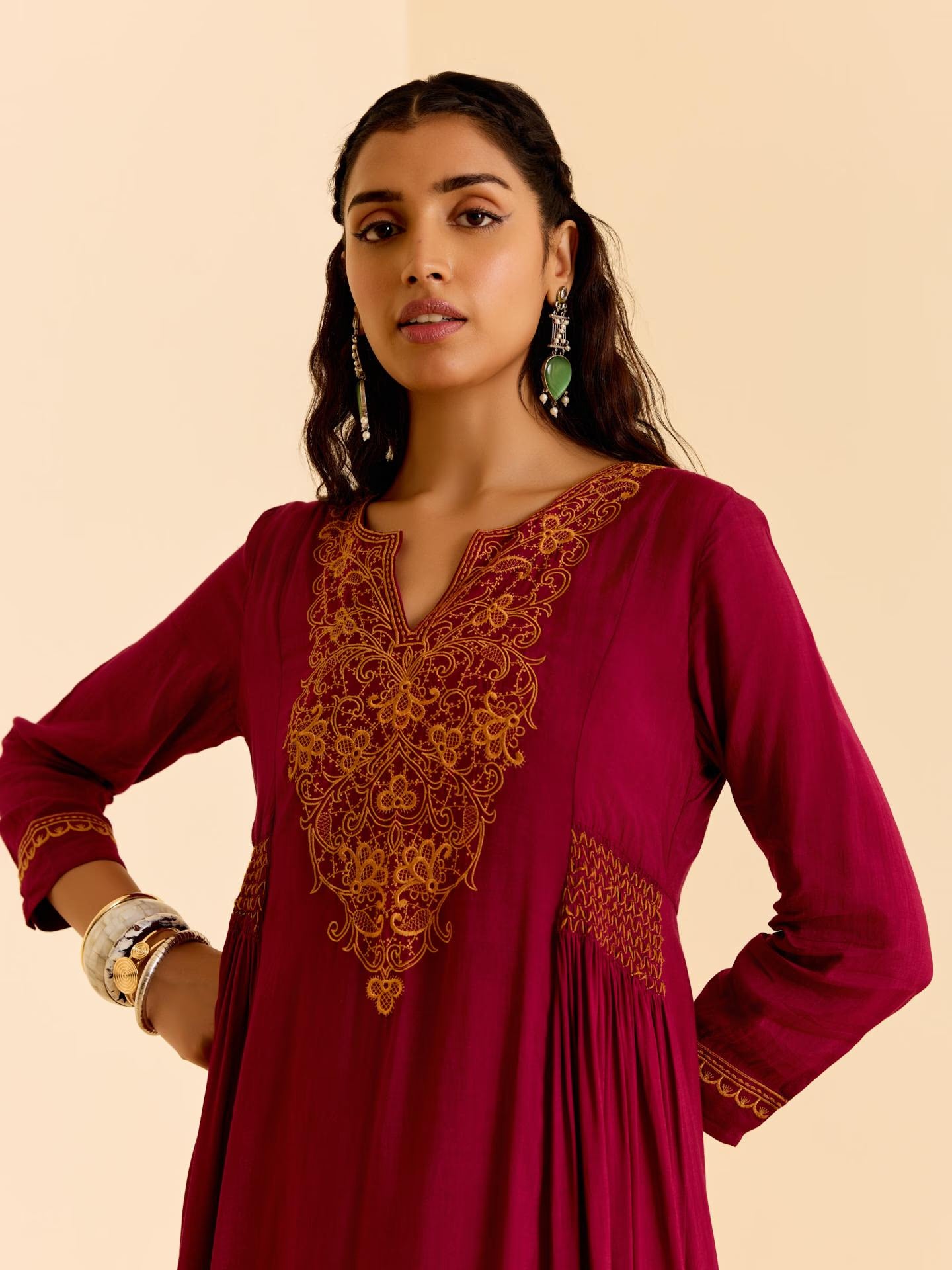Woman wearing a maroon traditional outfit with gold embroidery on a beige background