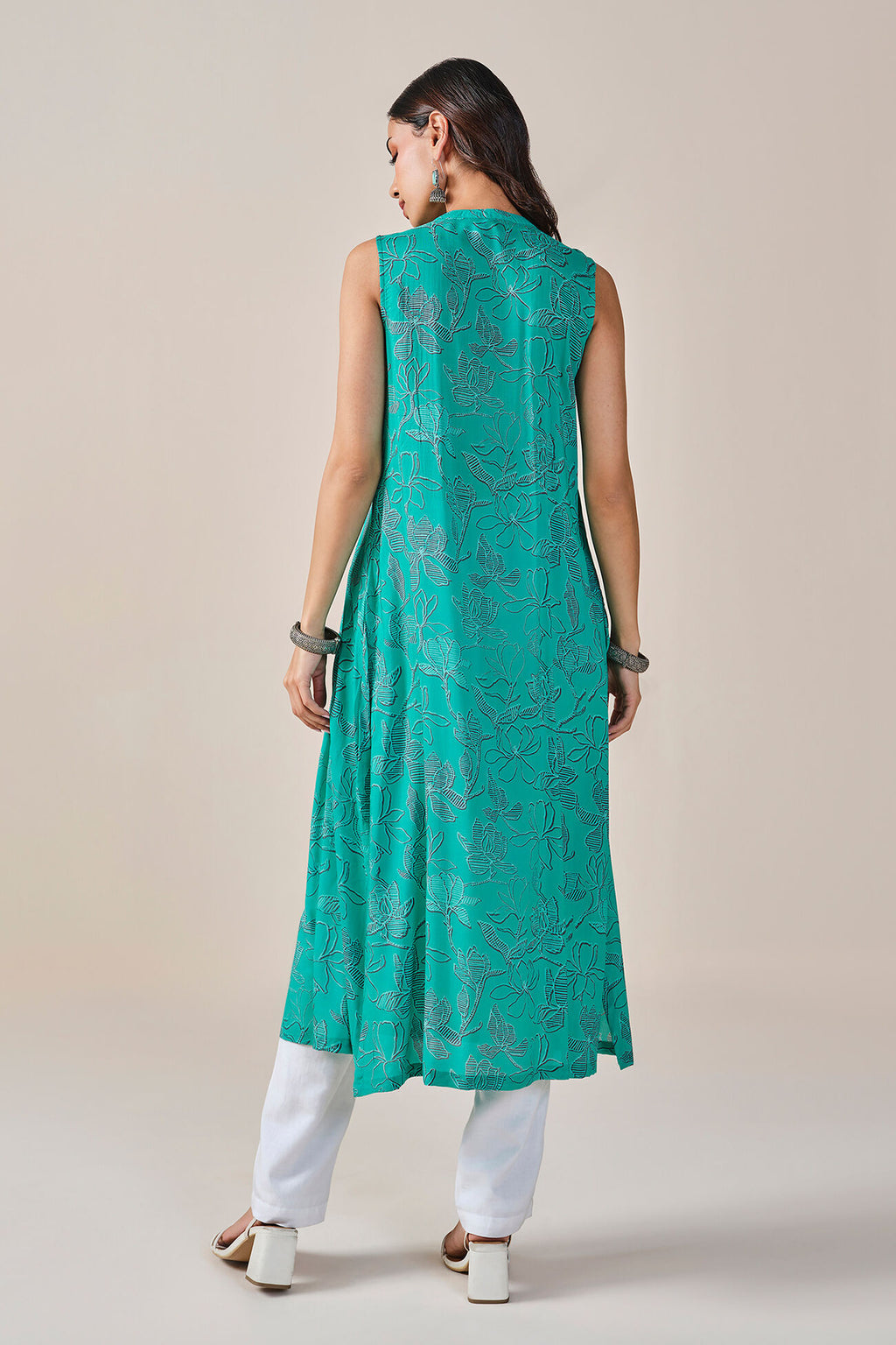 Woman wearing a teal sleeveless kurta with white pants on a beige background