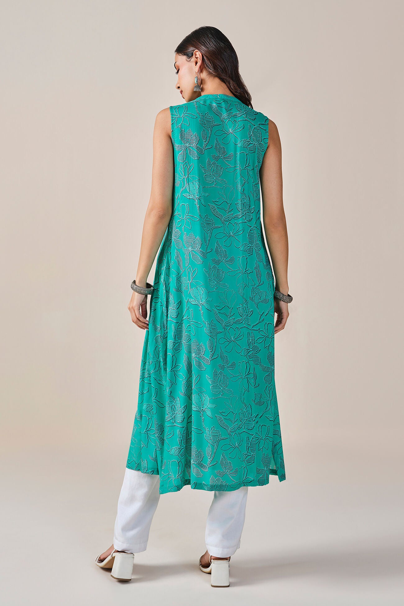 Woman wearing a teal sleeveless kurta with white pants on a beige background