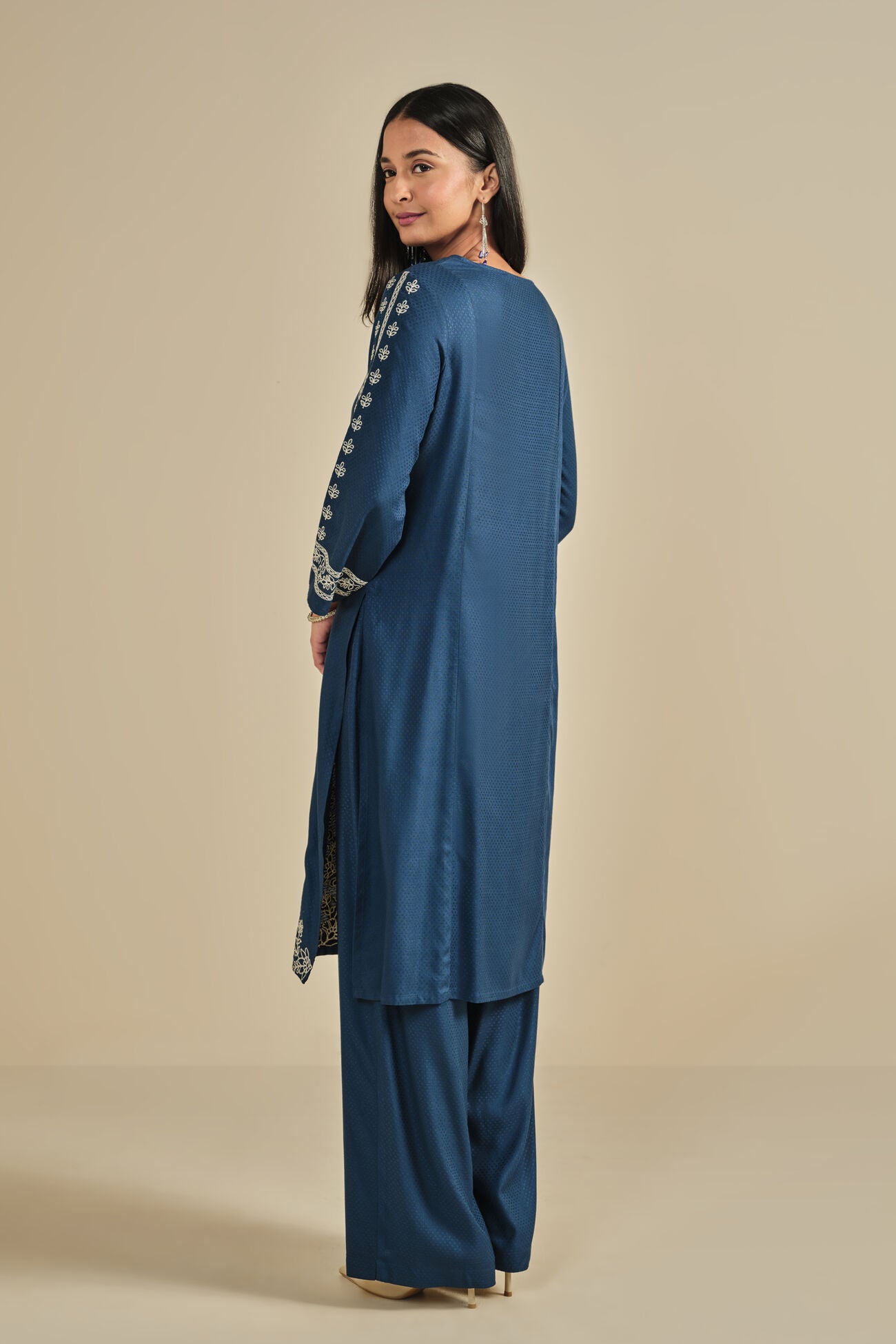 Woman wearing a blue traditional outfit with embroidery on a beige background