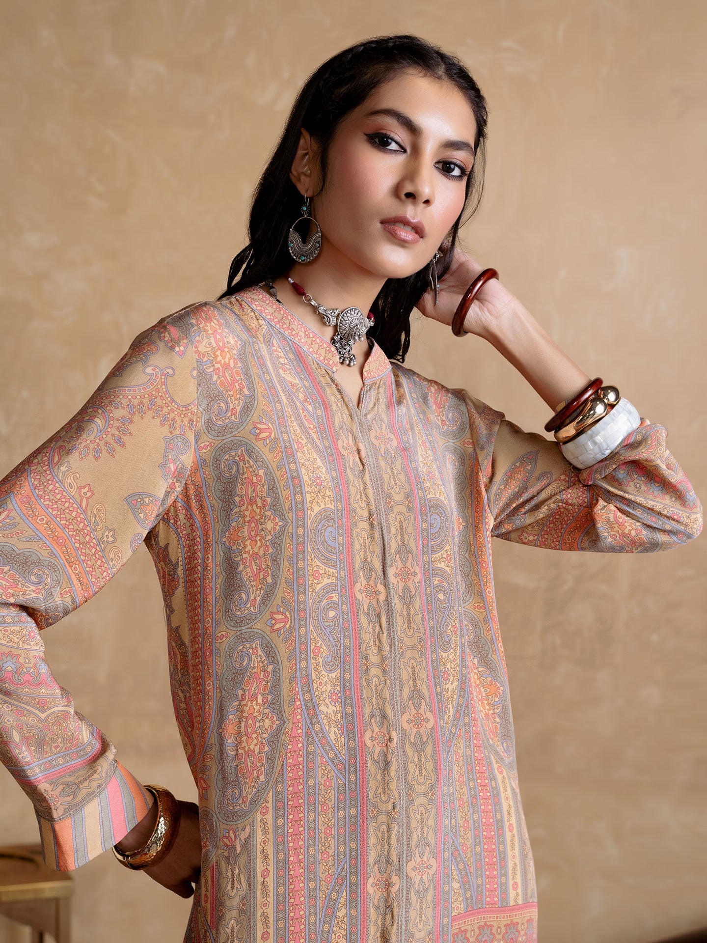 Woman wearing a patterned kurta with jewelry against a beige background