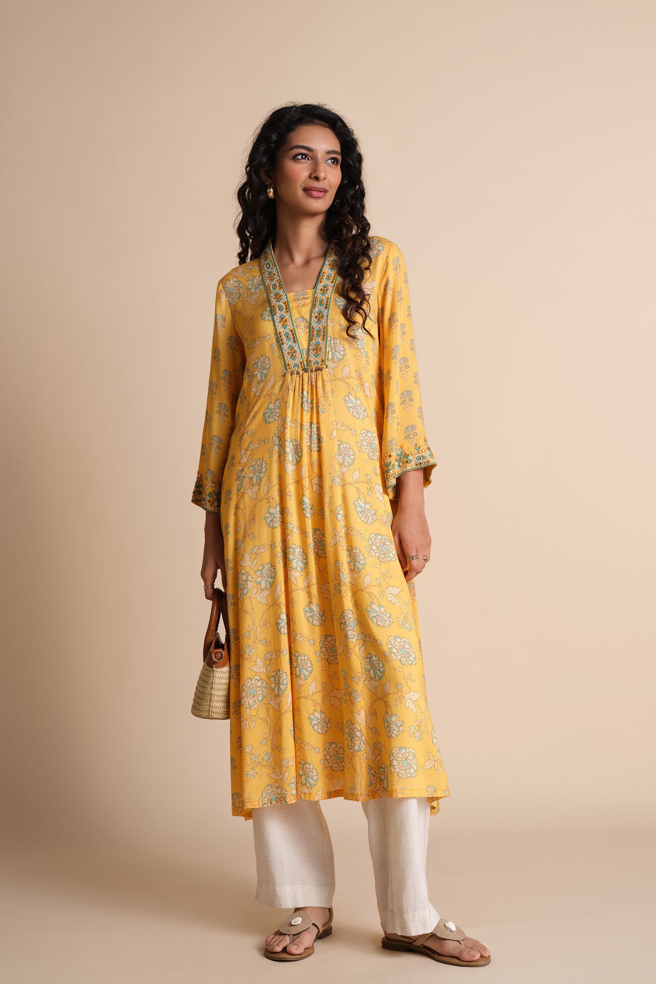 Woman wearing a yellow kurta with white pants on a beige background