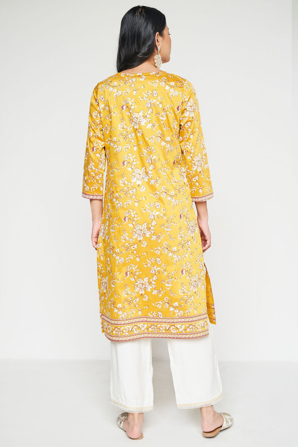 Woman wearing a yellow floral kurta with white pants on a white background