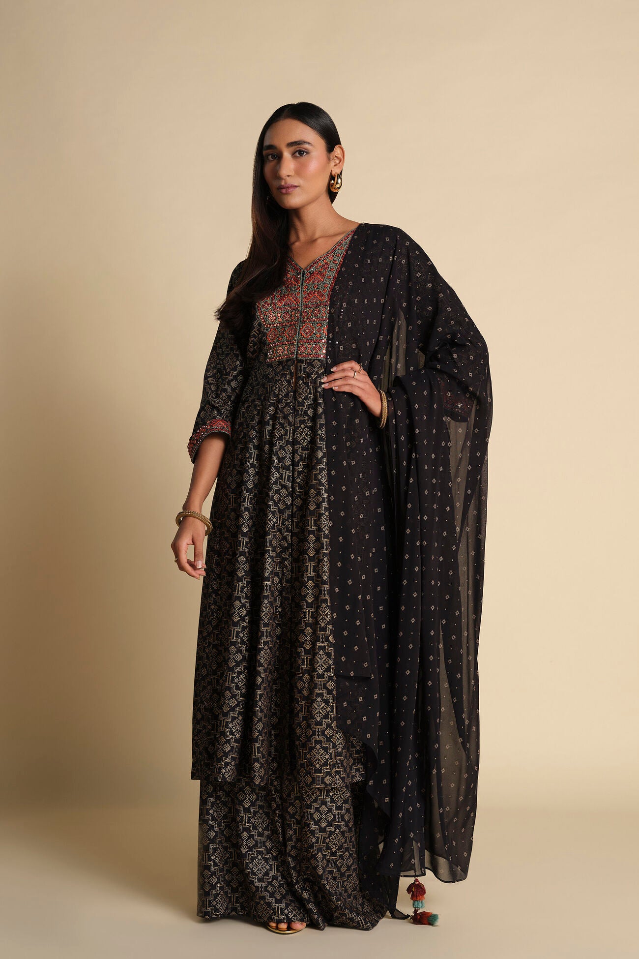 Woman wearing a long, dark patterned dress with a matching shawl against a beige background