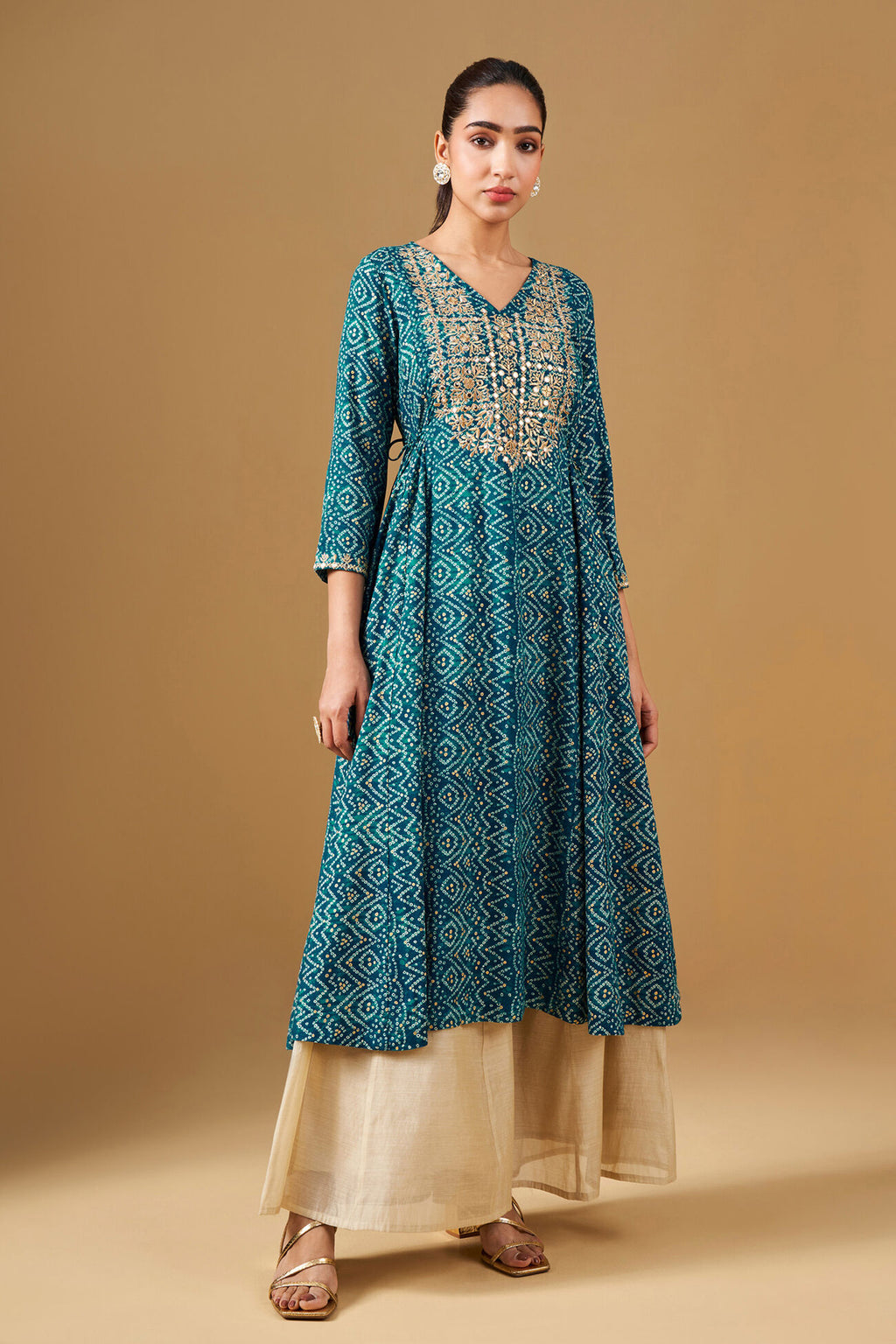 Woman wearing a teal patterned kurta with beige pants on a beige background