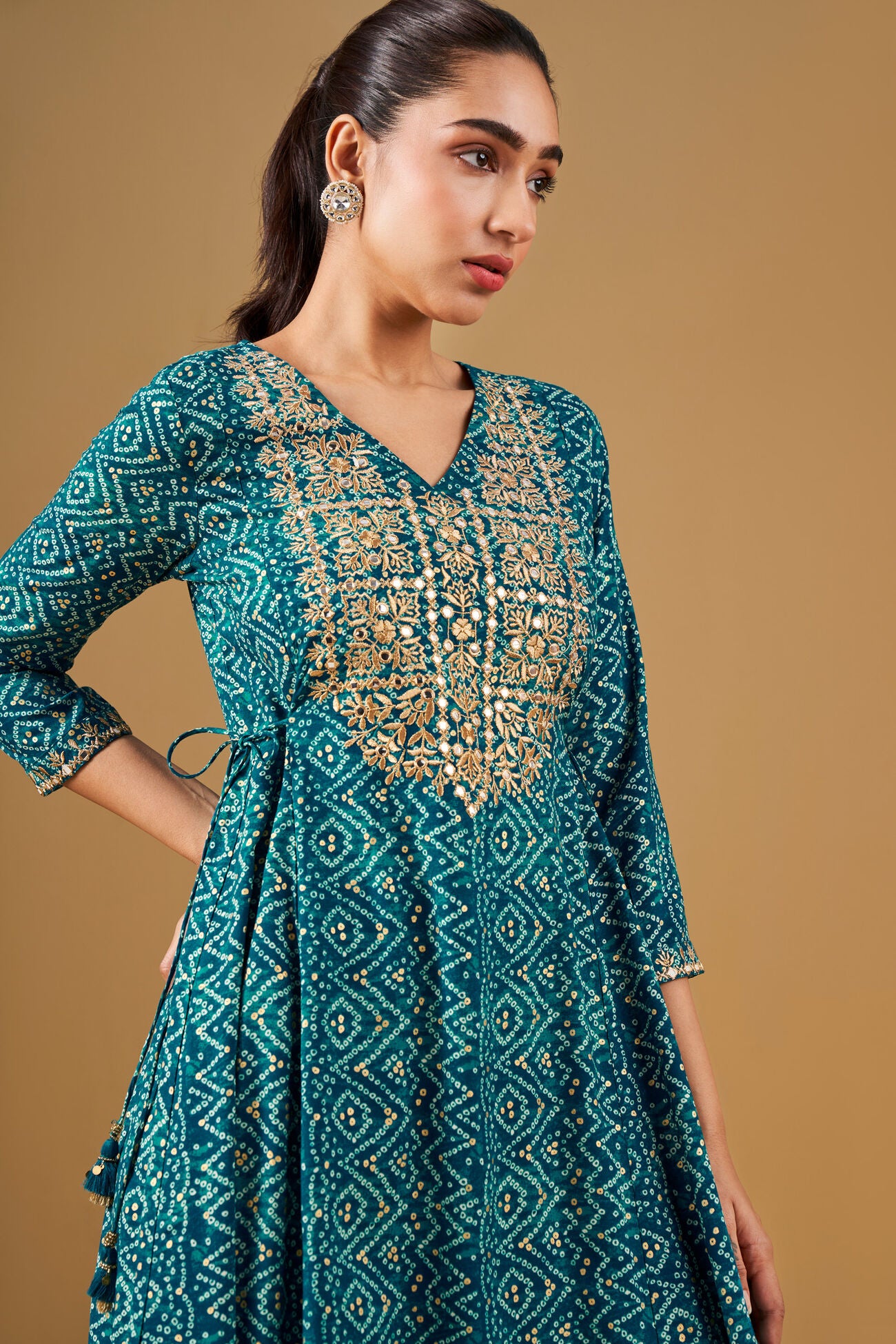 Woman wearing a teal embroidered dress against a beige background