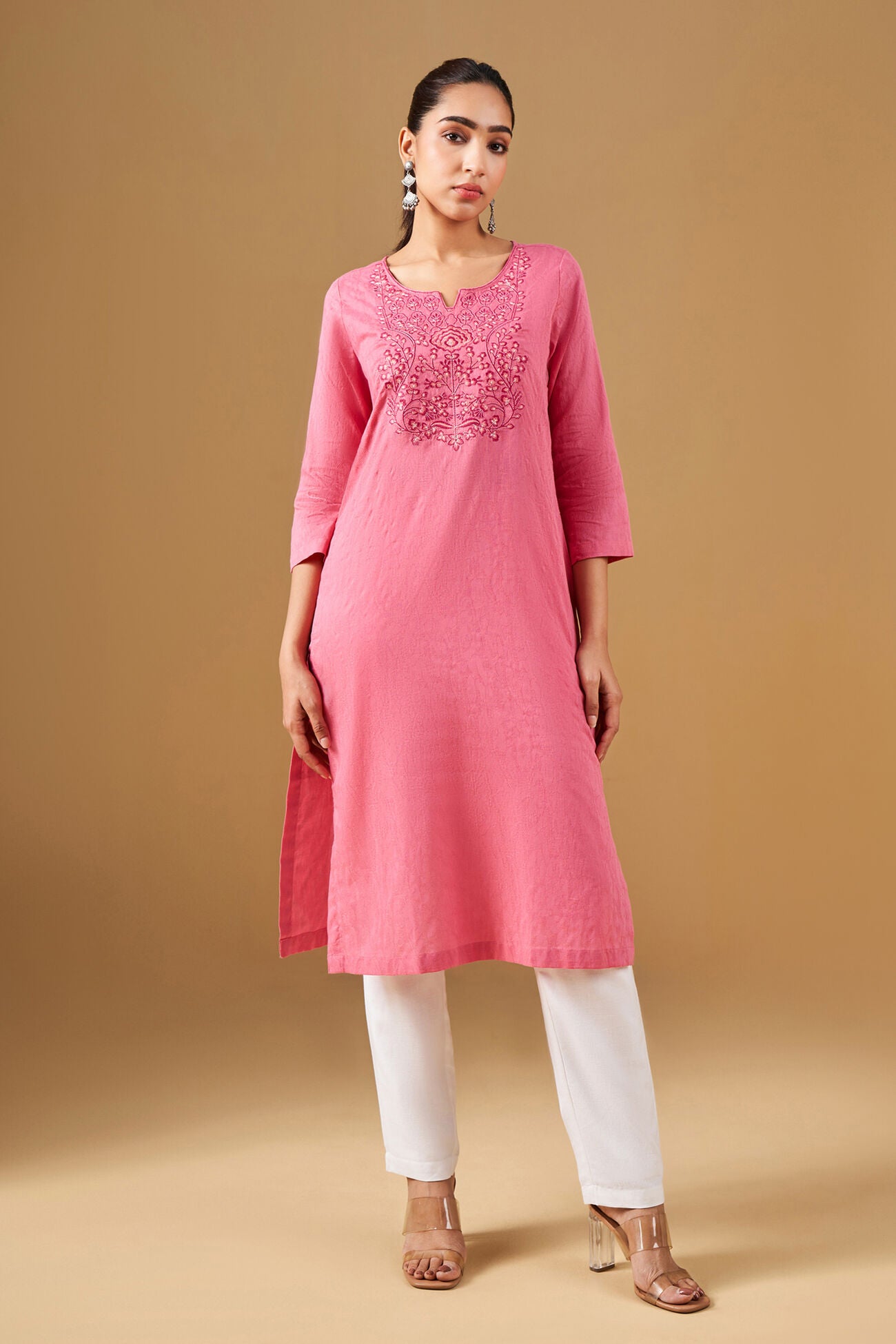 Woman wearing a pink kurta with white pants on a beige background