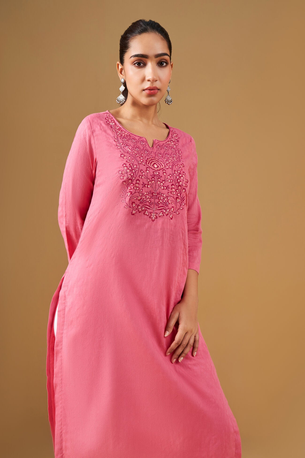 Woman wearing a pink embroidered kurta against a brown background