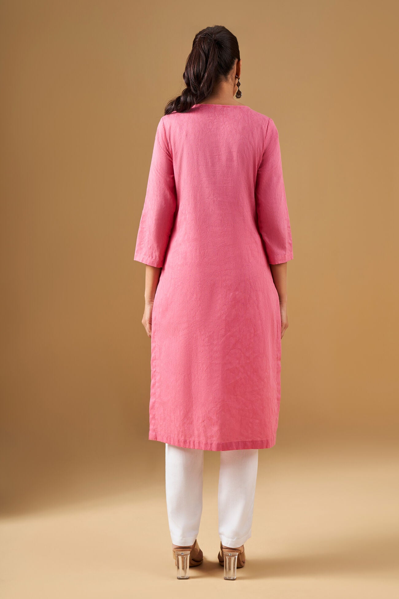 Woman wearing a pink kurta with white pants on a beige background