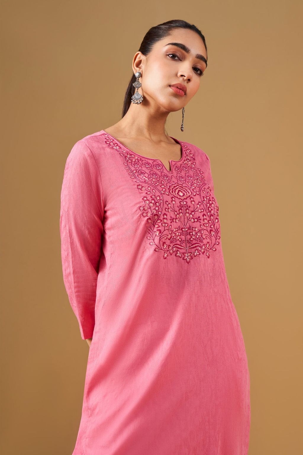 Woman wearing a pink embroidered dress against a brown background