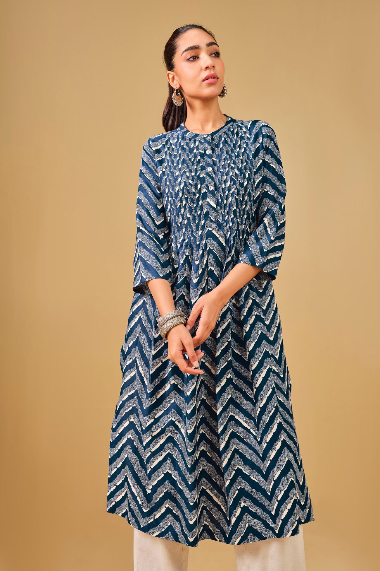 Woman wearing a blue patterned kurta with white pants on a beige background