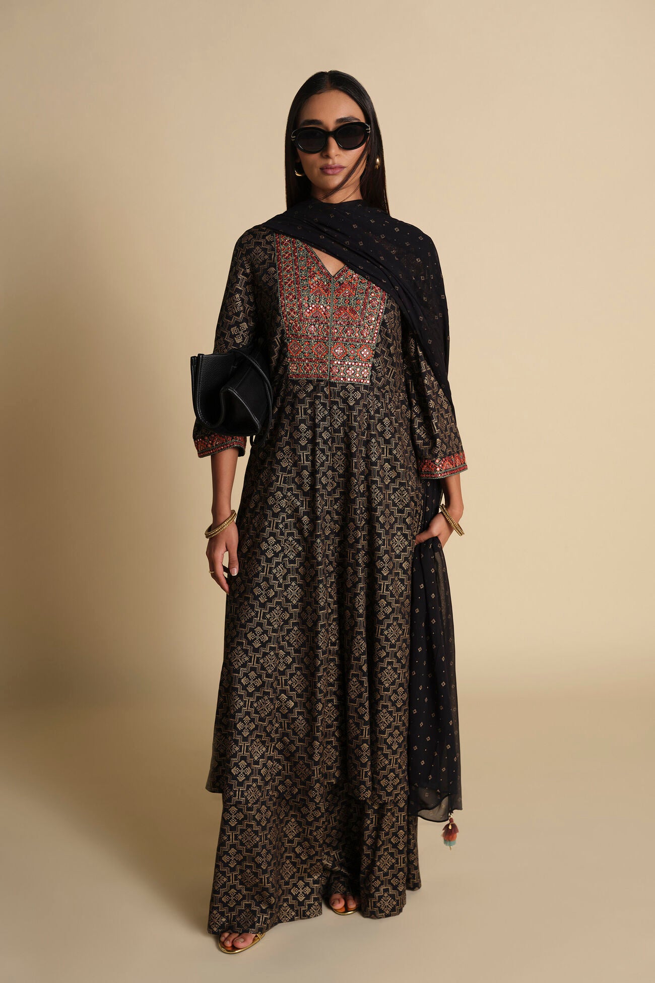 Woman wearing a long, patterned dress with a black hijab against a beige background