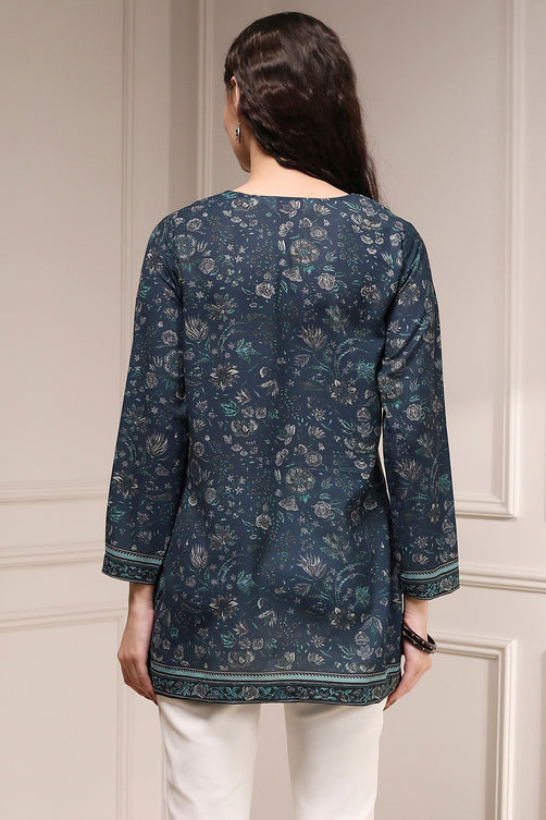 Woman wearing a dark floral patterned top against a neutral wall.