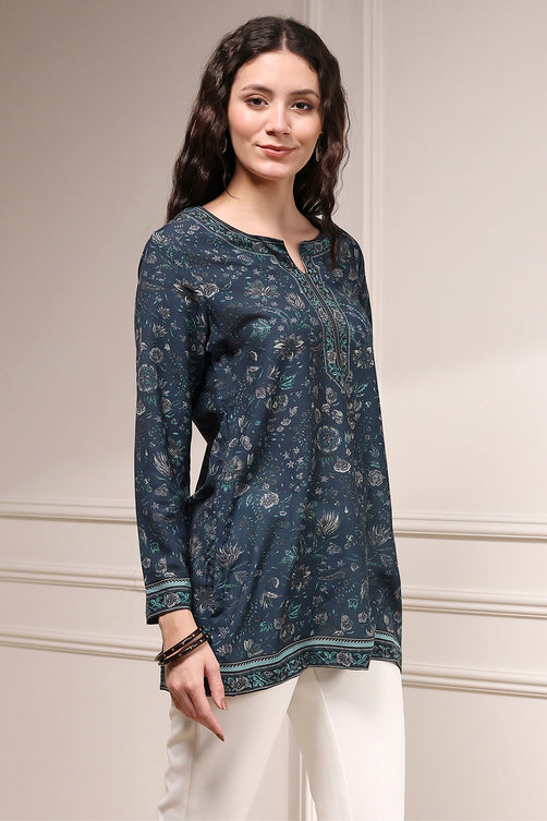 Woman wearing a dark blue floral patterned top with white pants against a neutral background