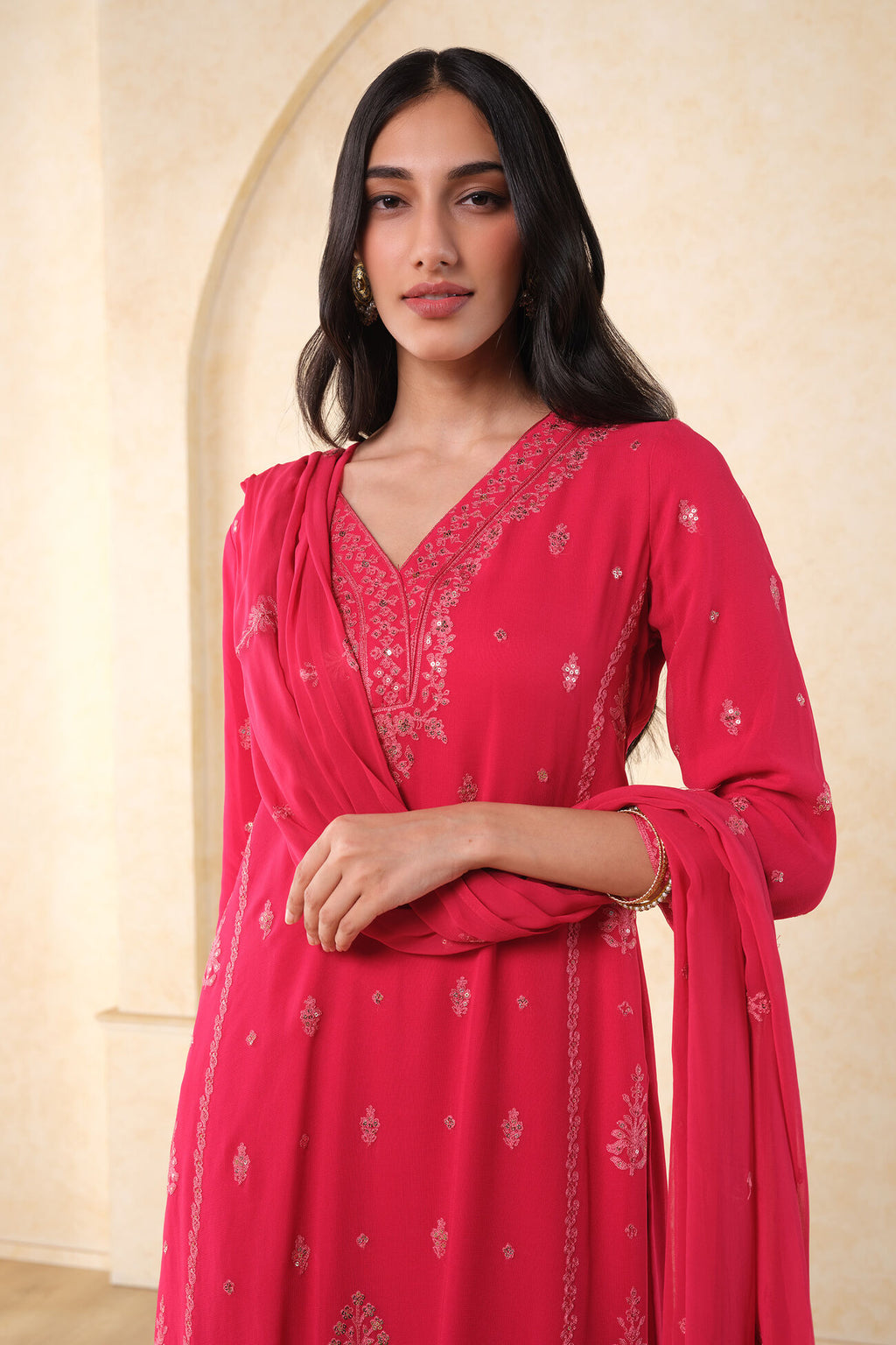 Woman wearing a pink traditional outfit with intricate designs against a beige background