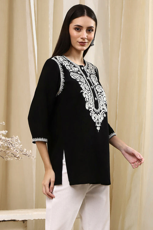 Woman wearing a black top with white embroidery against a beige curtain background