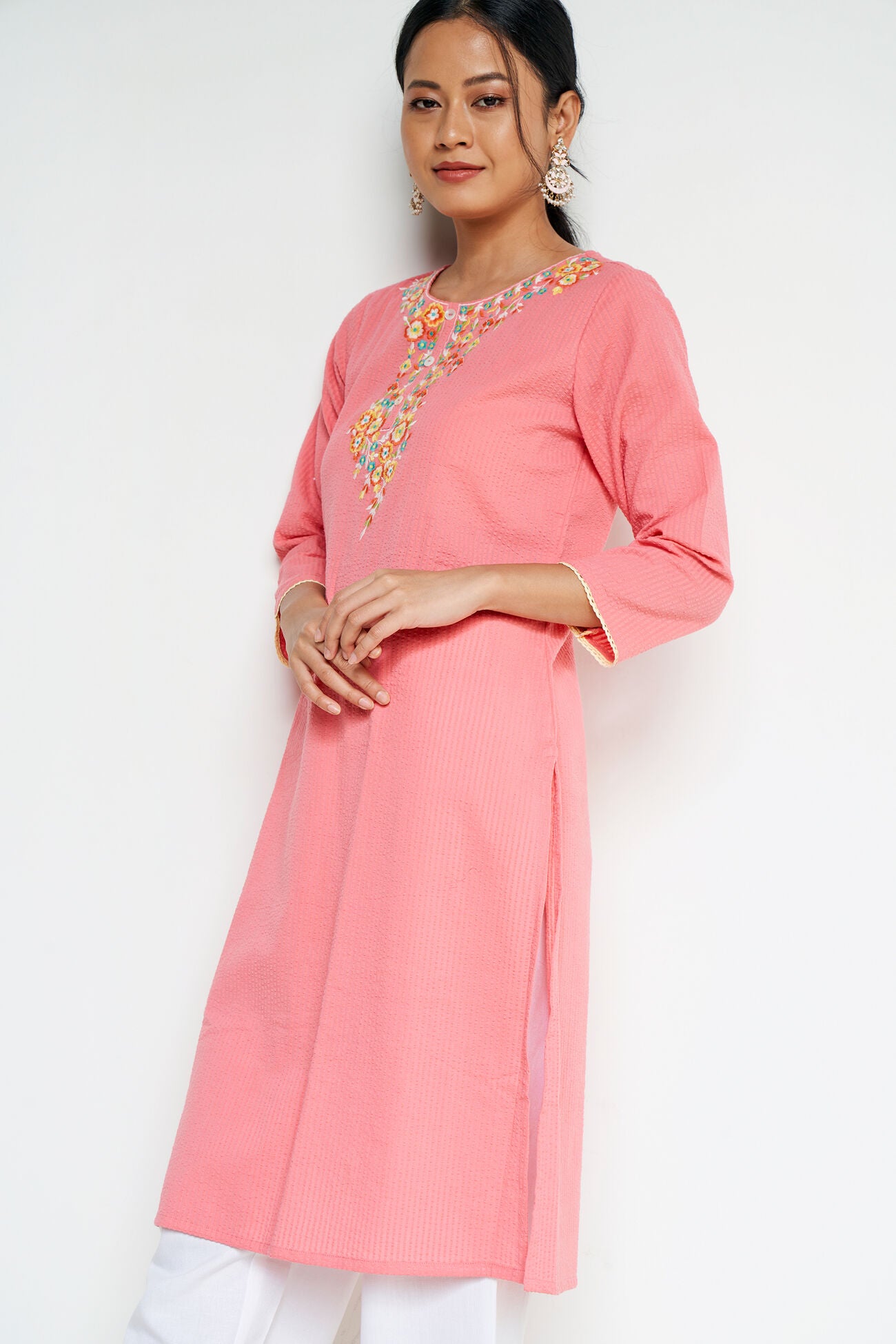 Woman wearing a pink kurta with white pants on a plain background