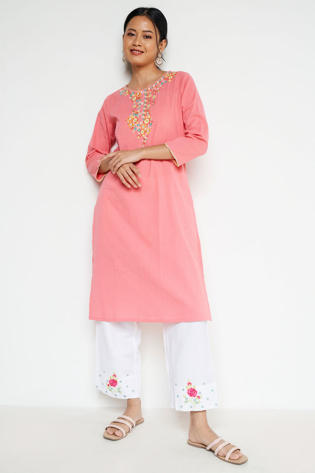 Woman wearing a pink embroidered kurta with white pants on a white background