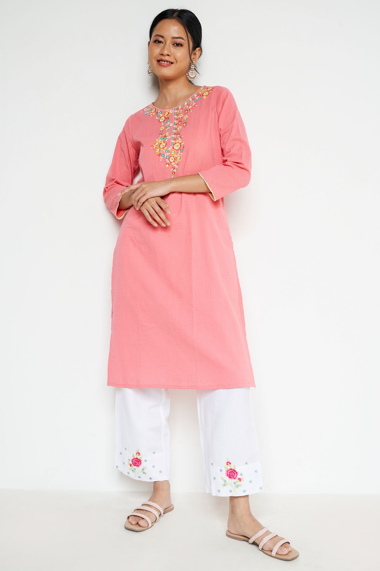 Woman wearing a pink embroidered kurta with white pants on a white background