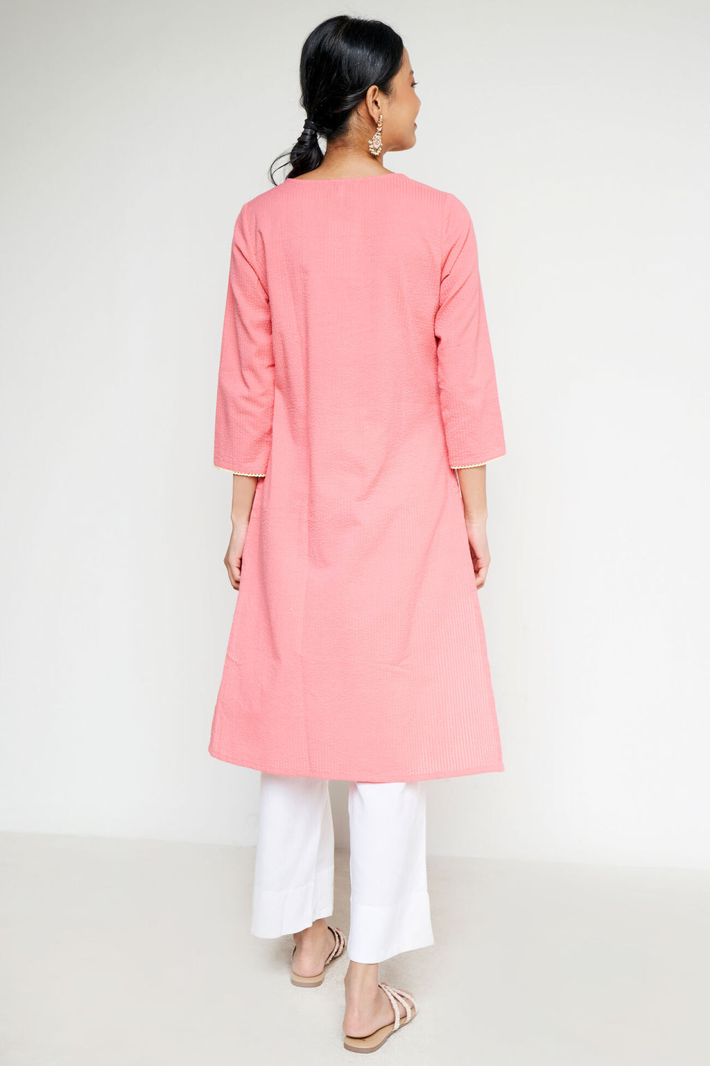 Woman wearing a pink kurta with white pants on a white background