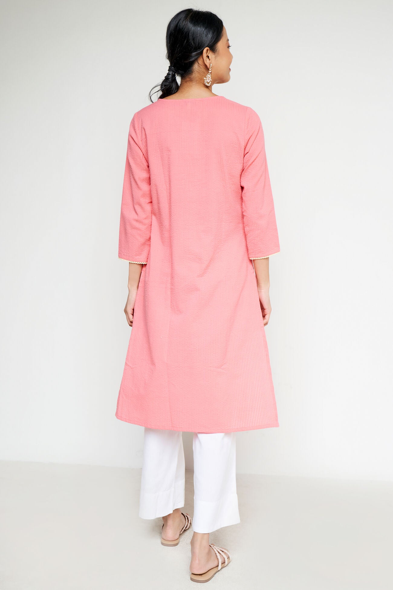 Woman wearing a pink kurta with white pants on a white background