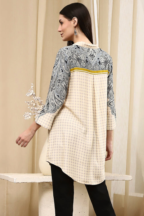 Woman wearing a patterned top with a checkered design, standing against a neutral background.