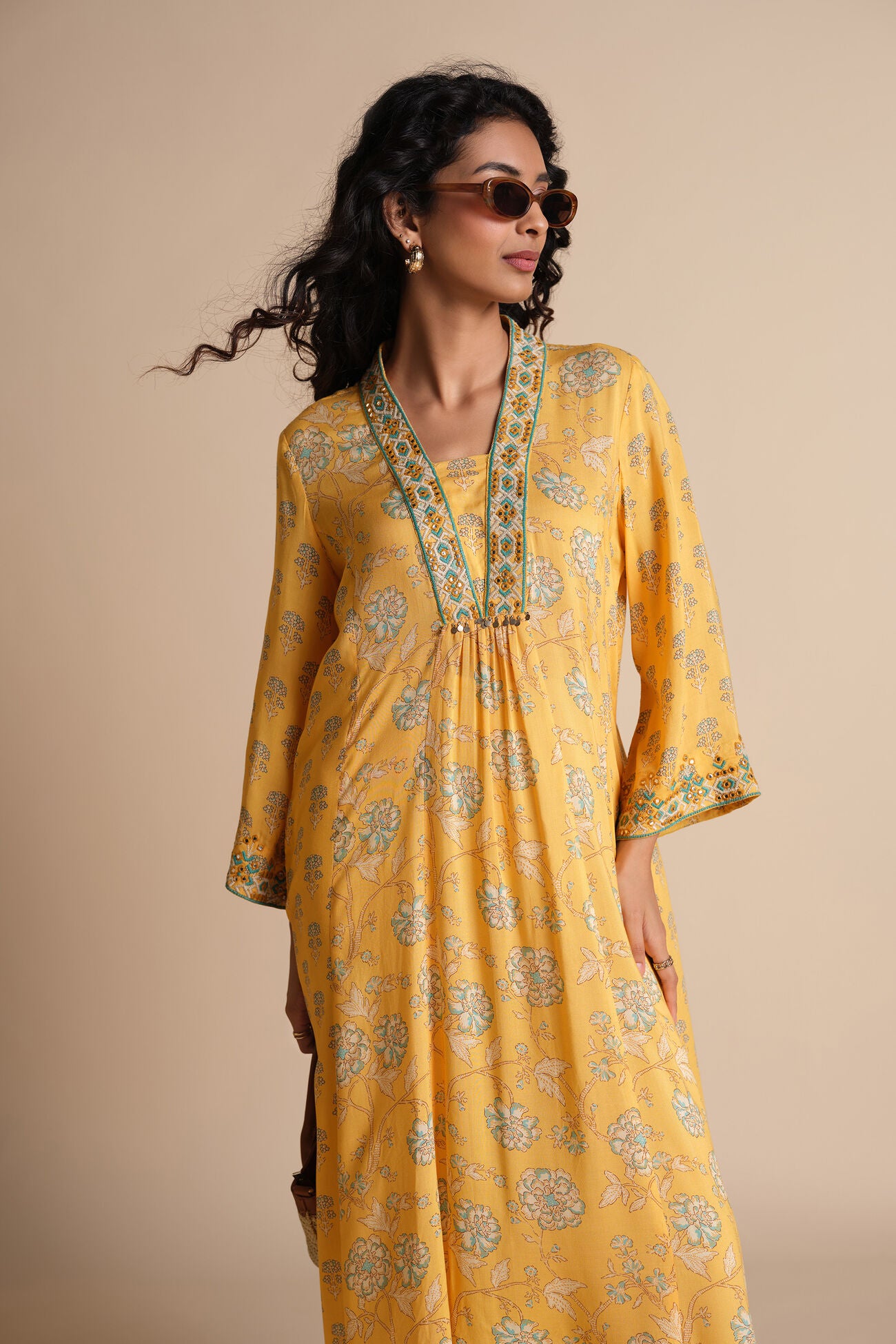Woman wearing a yellow floral dress against a beige background