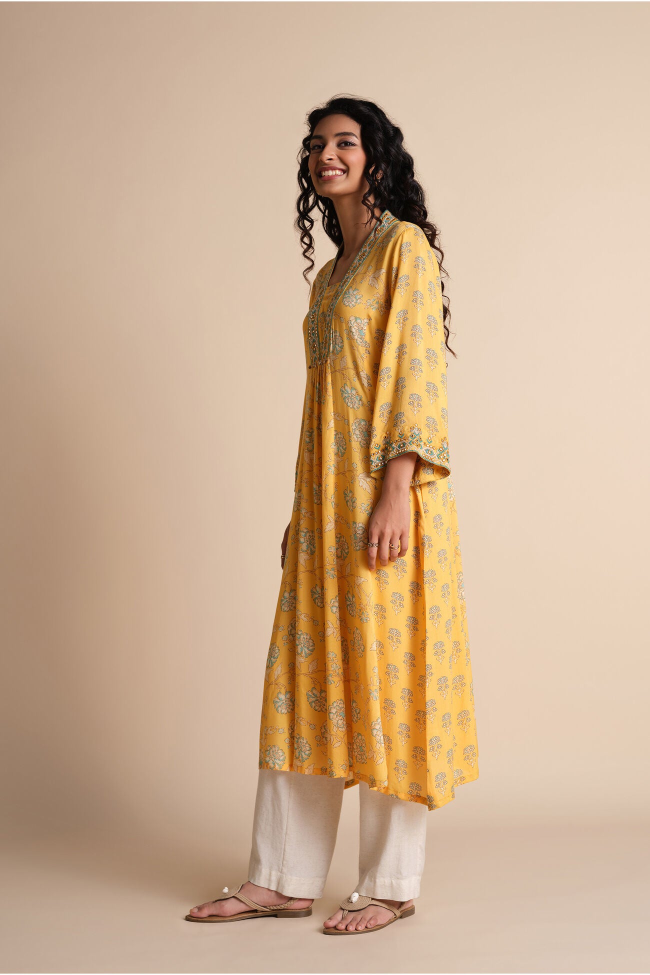 Woman wearing a yellow kurta with white pants on a beige background