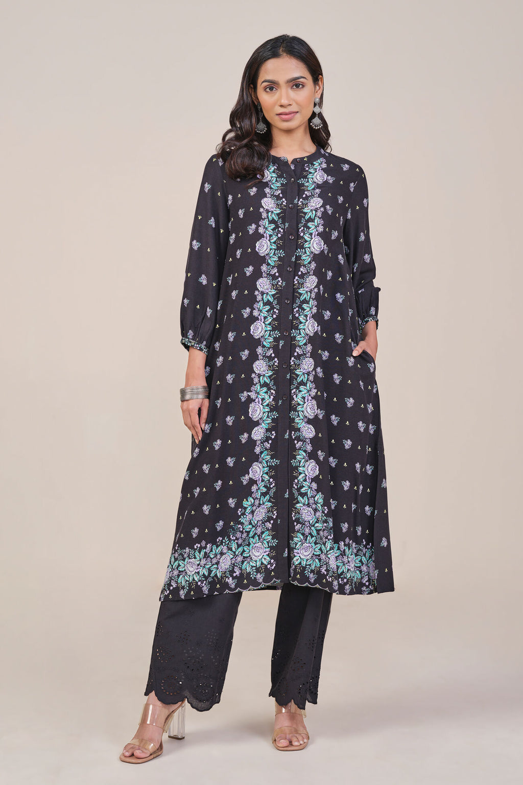 Woman wearing a black floral patterned kurta with black pants on a beige background