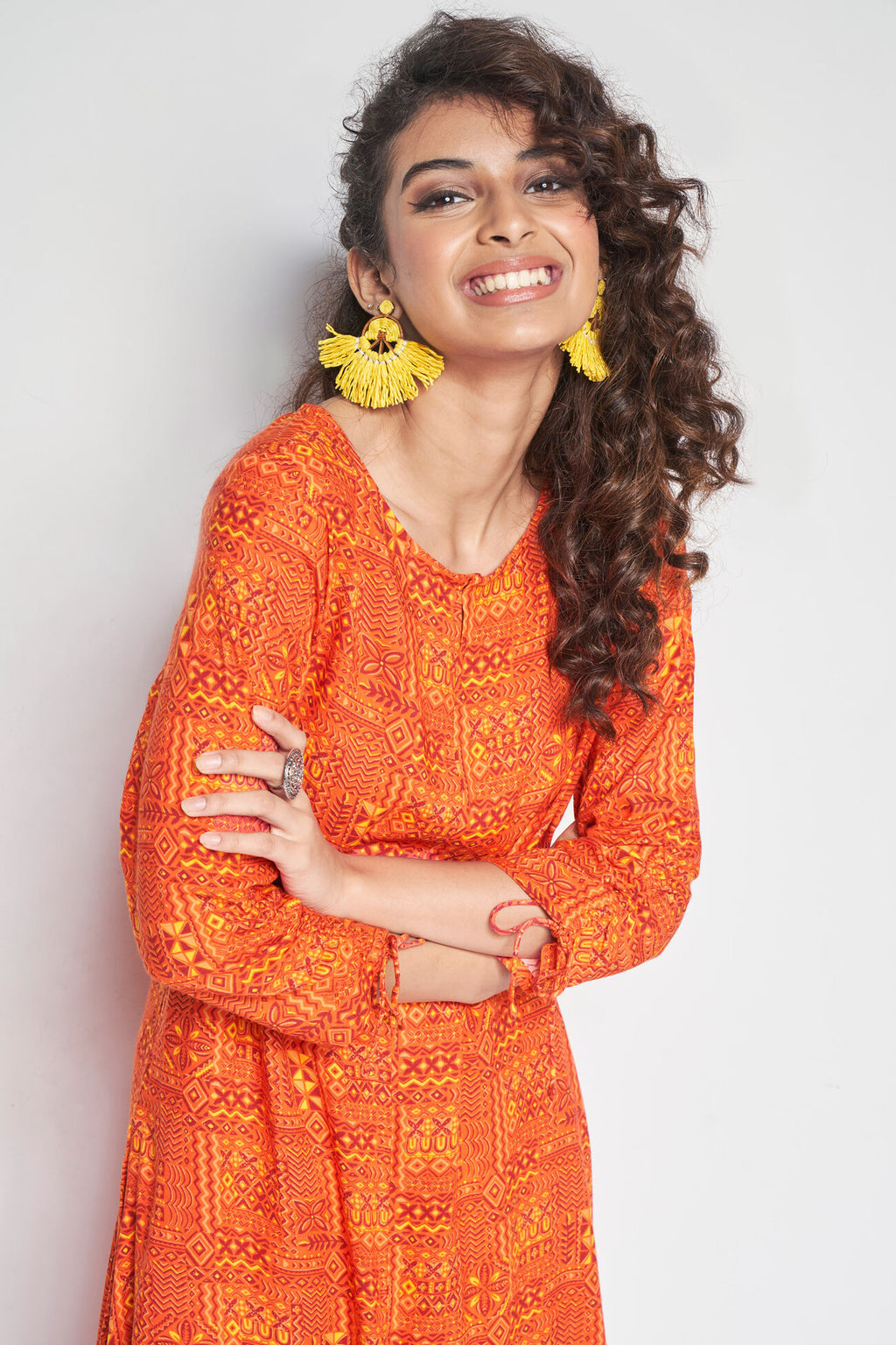 Woman wearing an orange patterned dress with yellow earrings on a white background