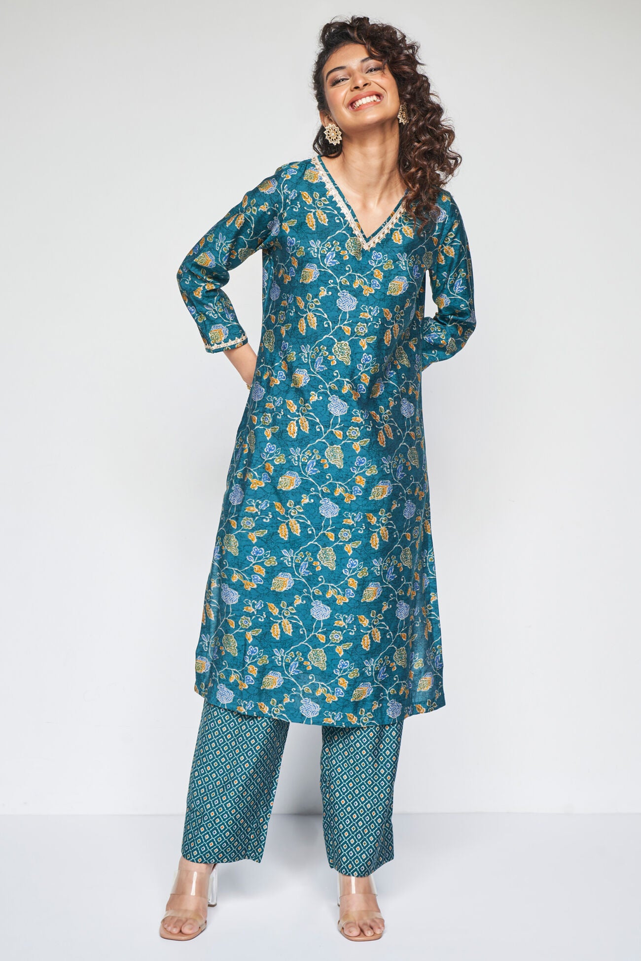 Woman wearing a teal floral kurta with matching pants on a white background