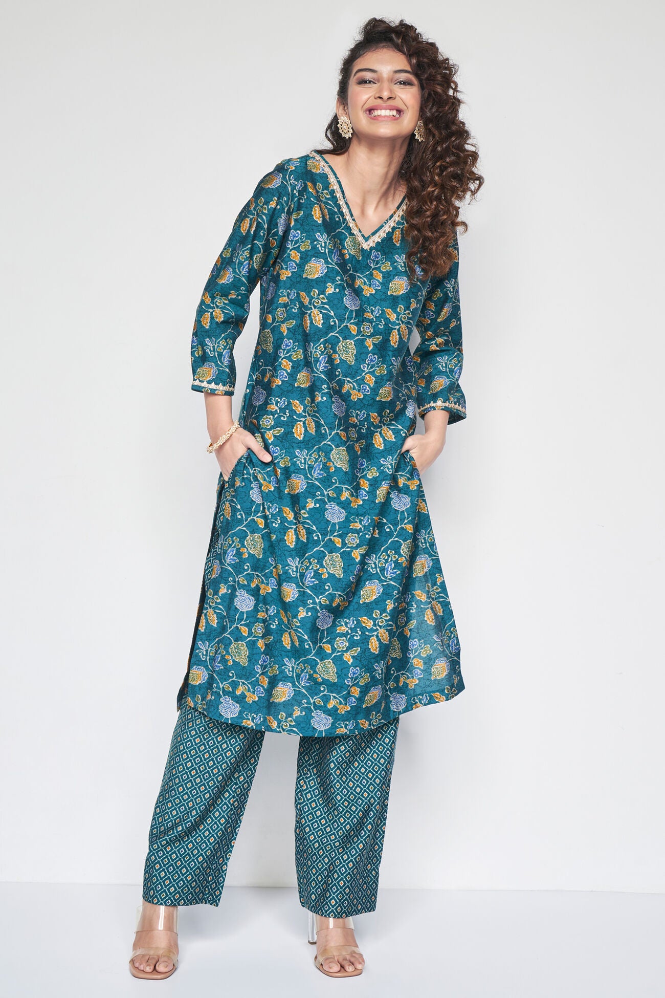 Woman wearing a teal floral kurta with matching pants on a white background