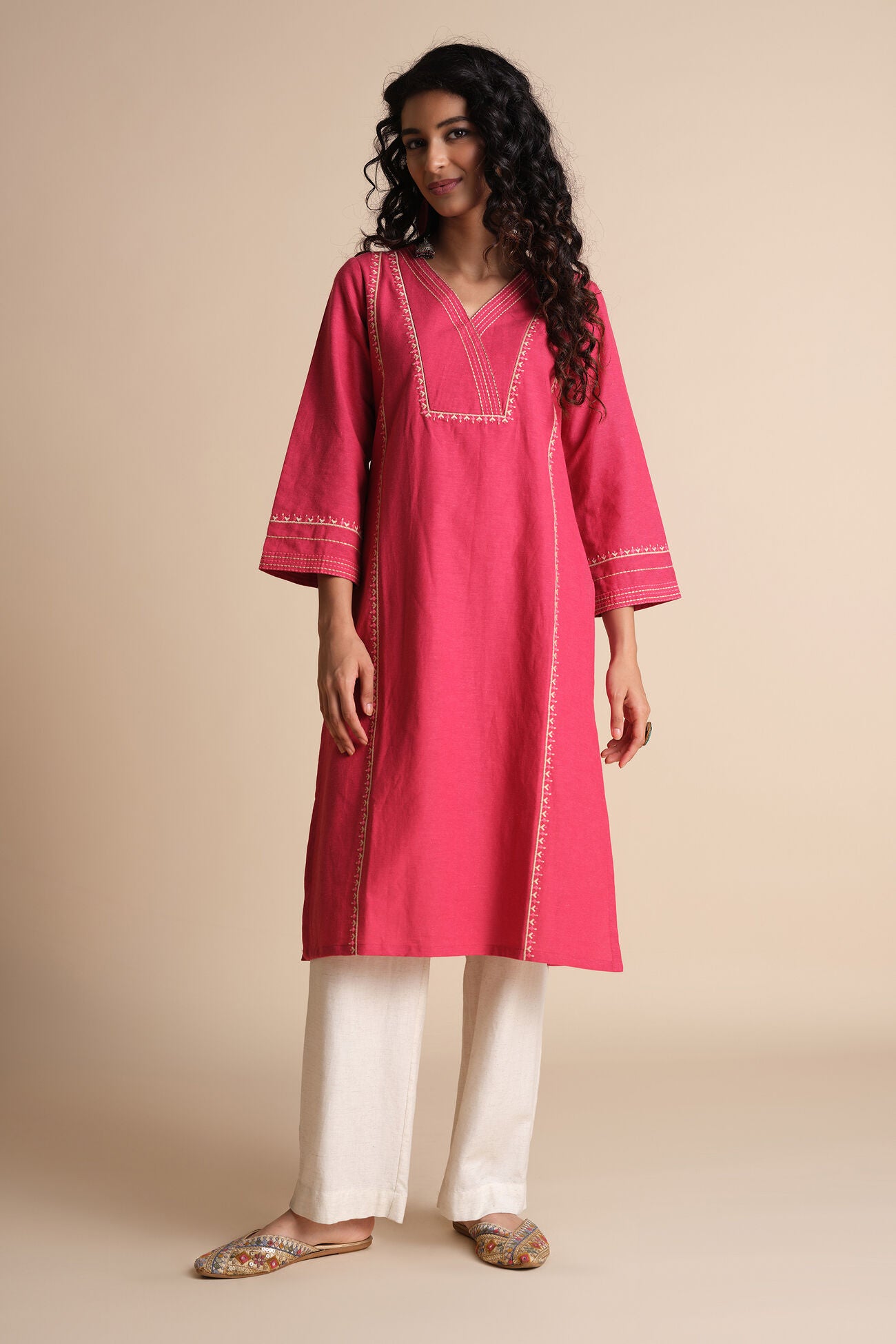 Woman wearing a pink kurta with white pants on a beige background