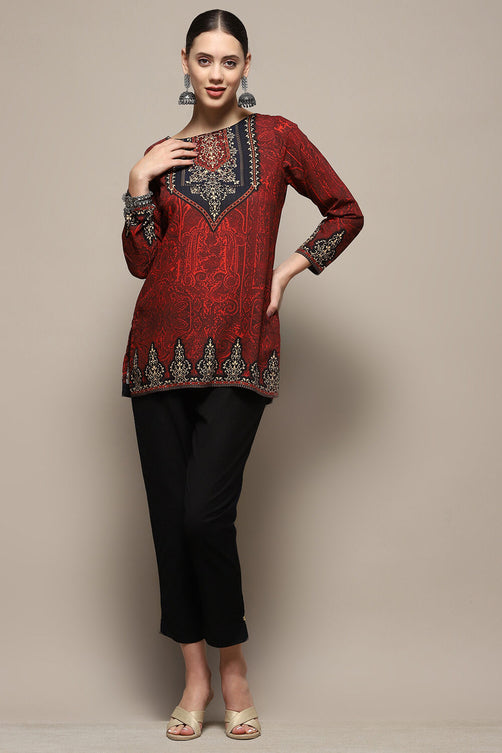 Woman wearing a red embroidered top and black pants on a beige background