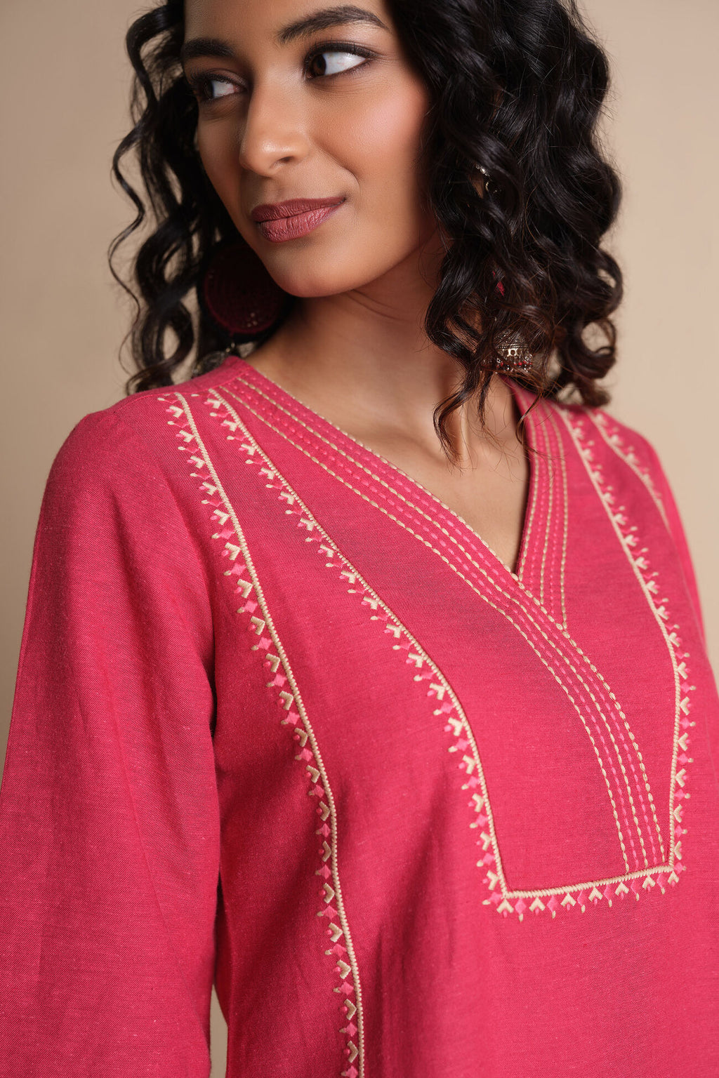 Woman wearing a pink embroidered top against a beige background