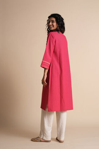 Woman wearing a bright pink kurta with white pants on a beige background