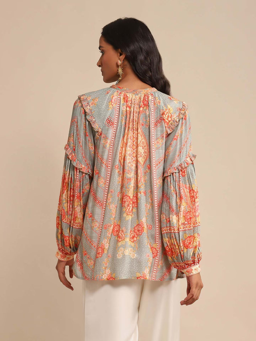 Woman in a multicolor printed high-neck kurta with full sleeves, paired with white straight pants and sandals, standing against a beige background