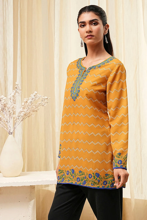 Woman wearing a yellow patterned top with black pants in a neutral setting