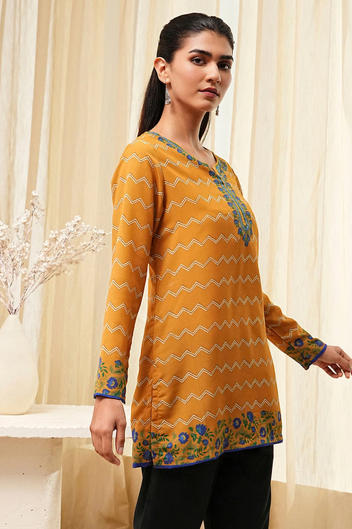 Woman wearing a yellow patterned top with black pants in a neutral setting