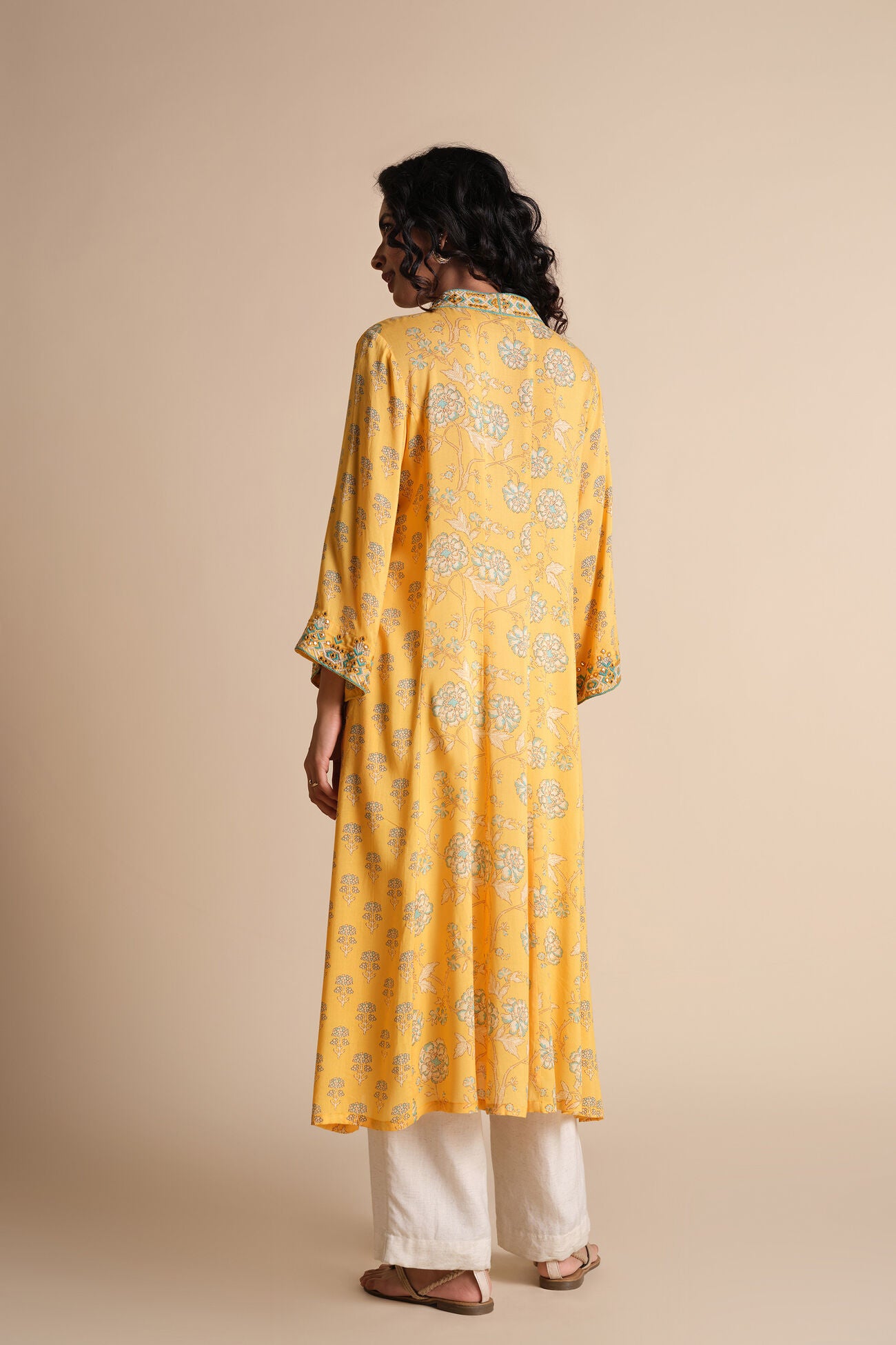 Woman wearing a yellow floral kurta with white pants on a beige background