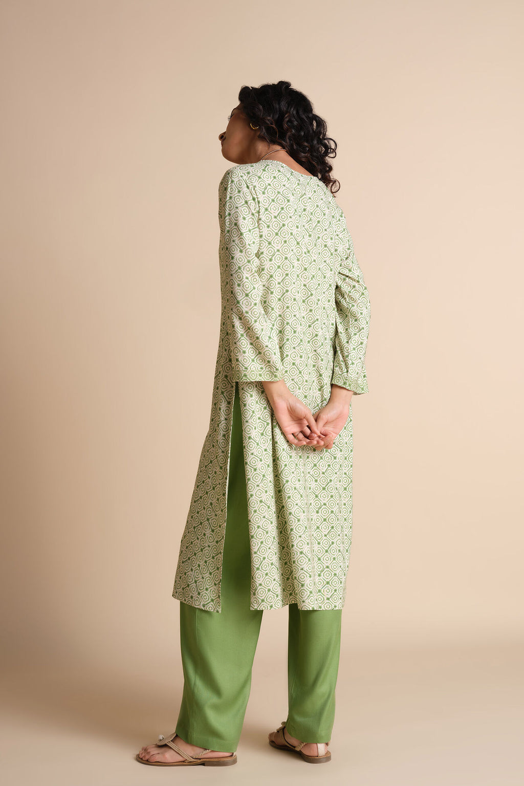 Person wearing a light green kurta with a subtle pattern and green pants on a beige background