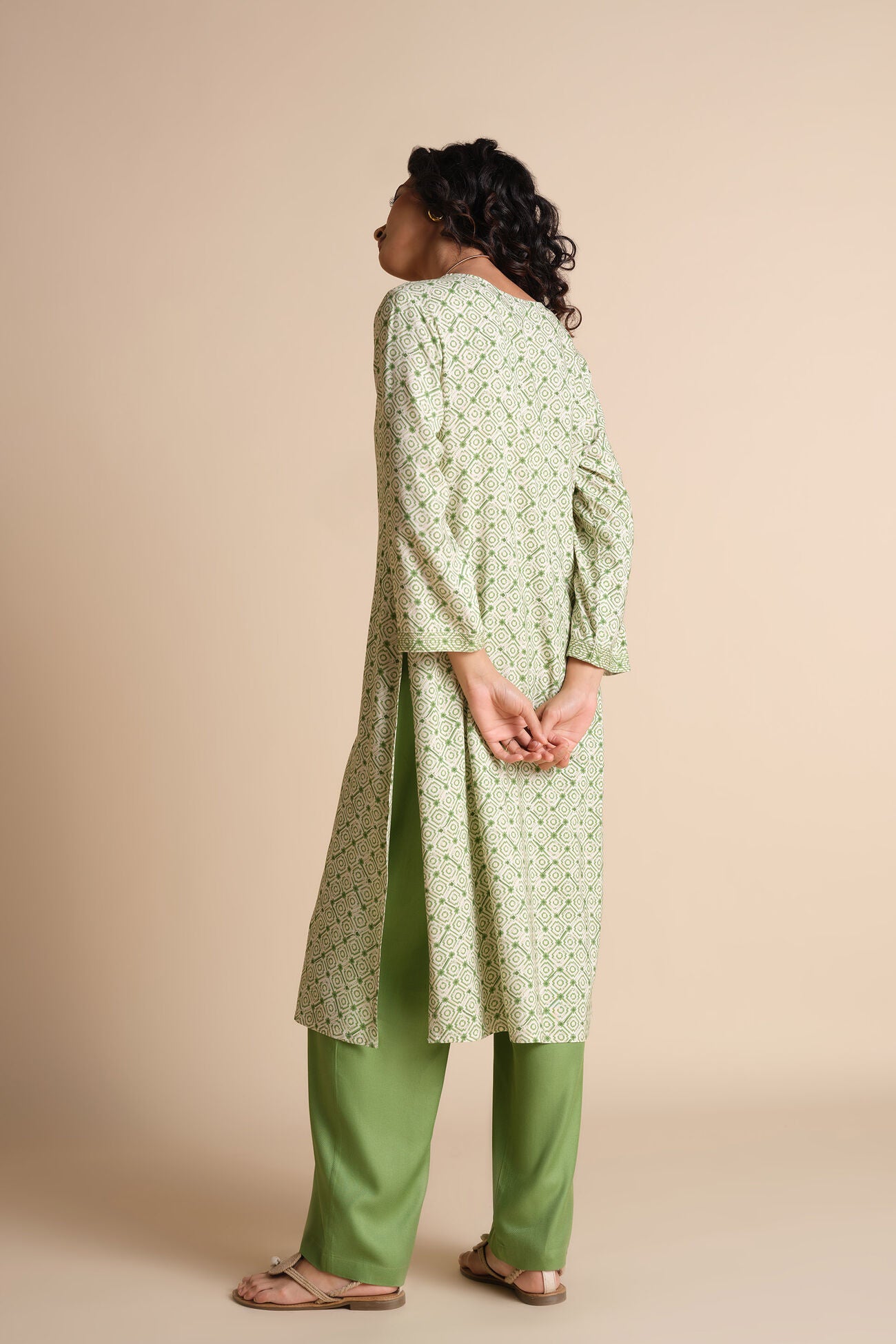 Person wearing a light green kurta with a subtle pattern and green pants on a beige background