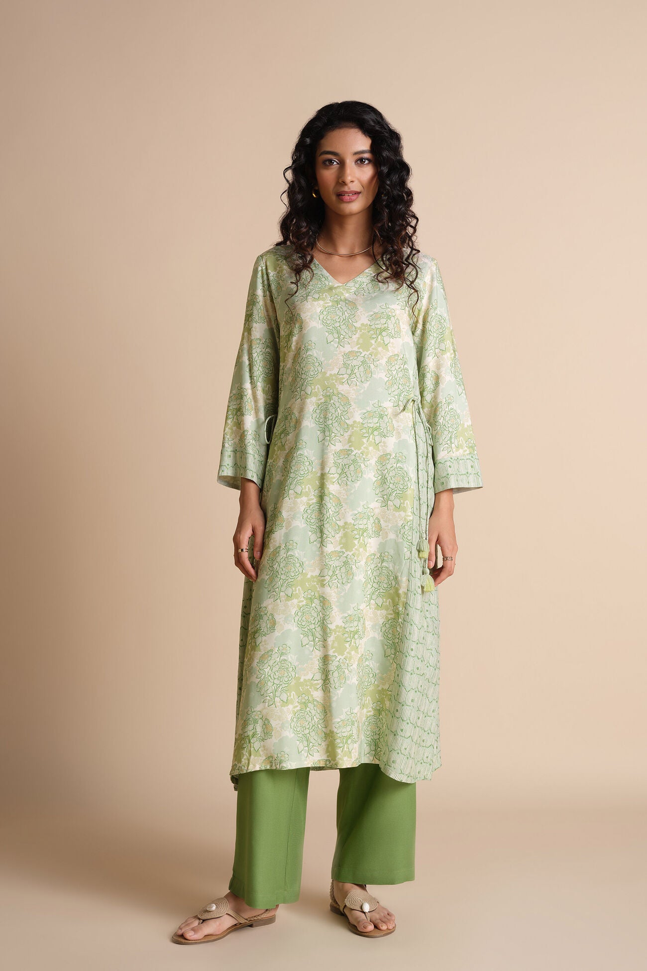 Woman wearing a green floral kurta with green pants on a beige background