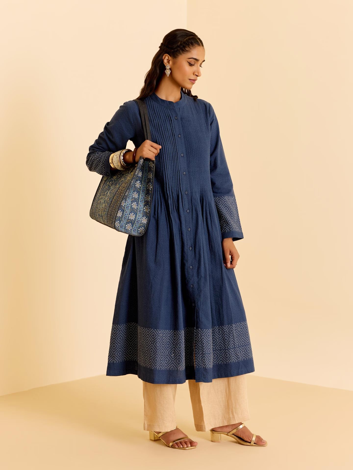 Woman wearing a blue dress holding a patterned bag on a beige background