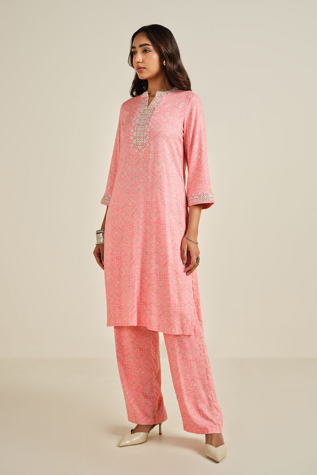 Woman wearing a pink traditional outfit with intricate patterns on a beige background