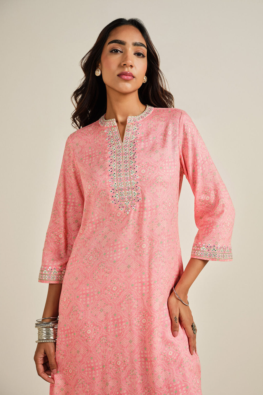 Woman wearing a pink traditional outfit with intricate designs on a beige background