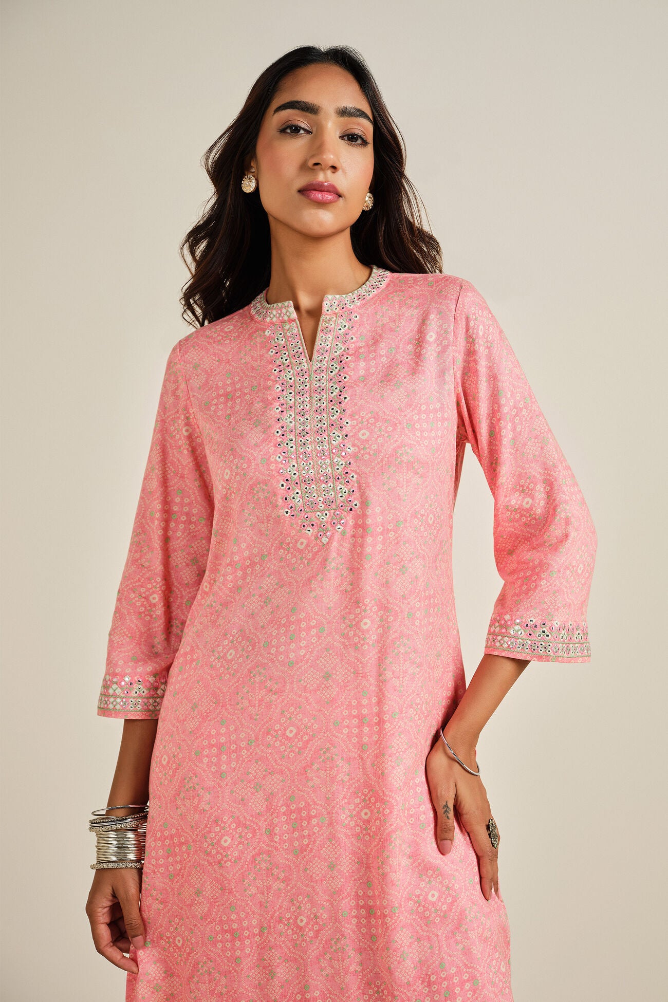 Woman wearing a pink traditional outfit with intricate designs on a beige background