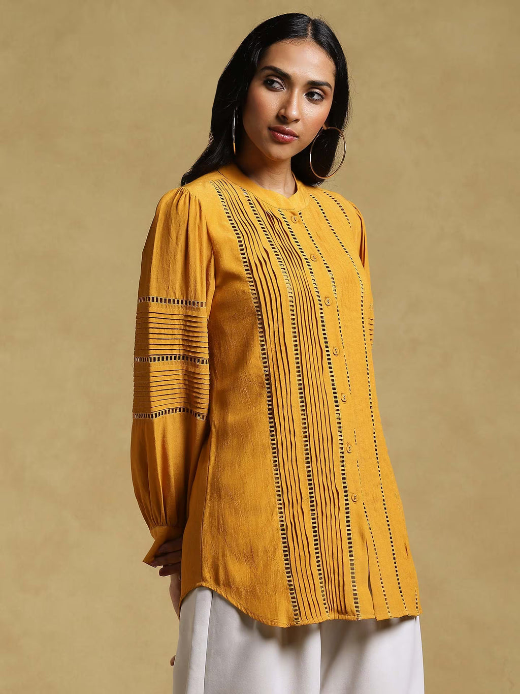 Woman wearing a mustard yellow blouse with black embroidery on a beige background