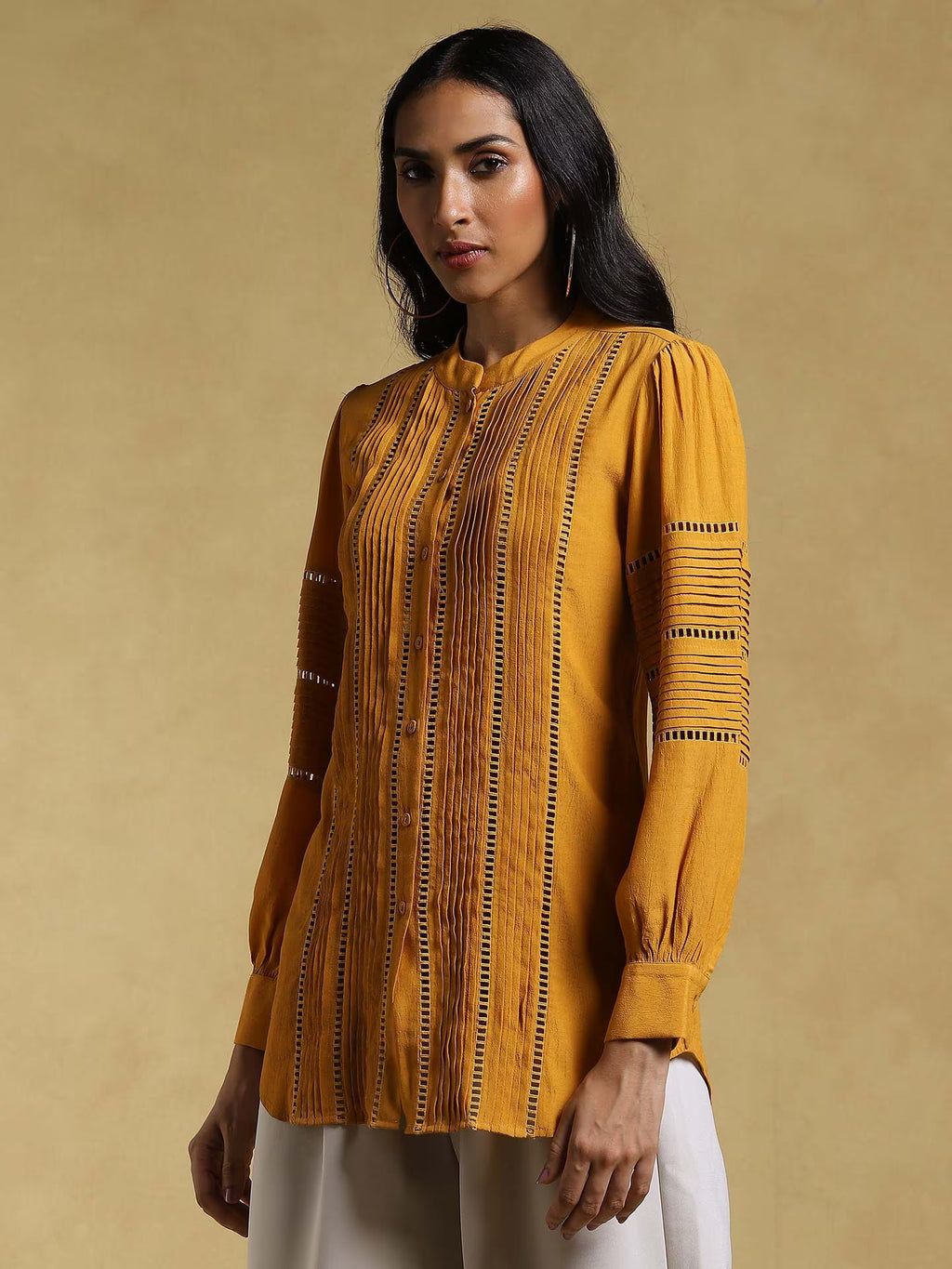 Woman wearing a mustard yellow patterned top against a beige background